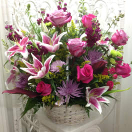 Basket arrangement of pink roses, lilies, and purple flowers