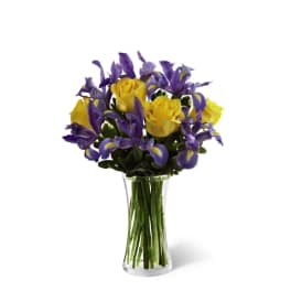 Yellow roses and purple irises in a clear glass vase