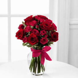 Red roses arranged in a clear glass vase with a pink ribbon
