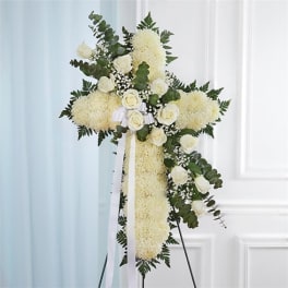 White floral cross arrangement on a stand with ribbon