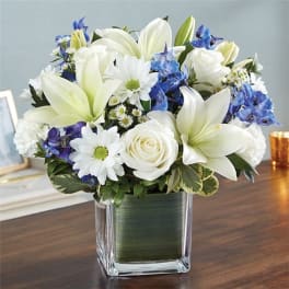 White lilies and roses with blue flowers in a glass vase
