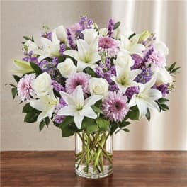 Bouquet of white lilies, roses, and purple flowers in a glass vase