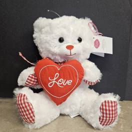 White teddy bear holding a red heart pillow with the word Love