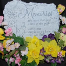 Decorative memorial plaque surrounded by colorful artificial flowers and a butterfly accent.