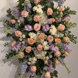 Large floral spray of peach roses, white blooms, and lavender flowers on an easel