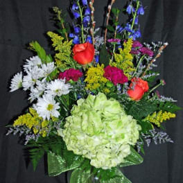 Mixed bouquet with hydrangea, roses, daisies, and blue flowers in a glass vase