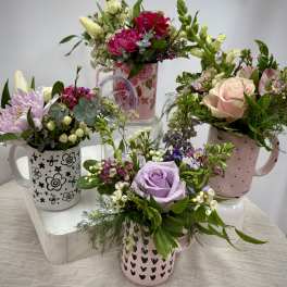 Four floral mug arrangements with roses, lilies, and mixed blooms in pastel mugs.