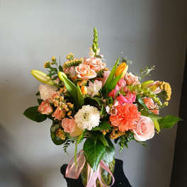 Mixed bouquet of pink roses, lilies, and carnations in a glass vase with a pink ribbon