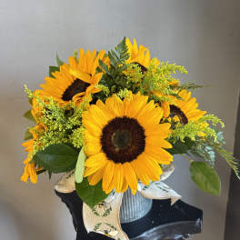 Bouquet of yellow sunflowers in a ribbed metal container with a ribbon