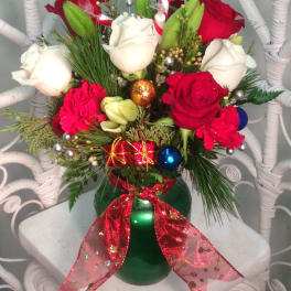 Red and white roses in a green vase with holiday ornaments and ribbon