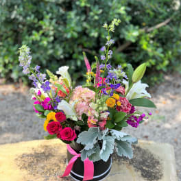 Colorful mixed flower arrangement in a black hatbox with a pink ribbon