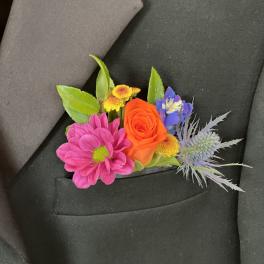 Colorful boutonniere with pink daisy, orange rose and mixed blooms in a black suit pocket