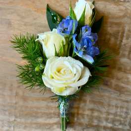 White rose boutonniere with blue flowers and greenery