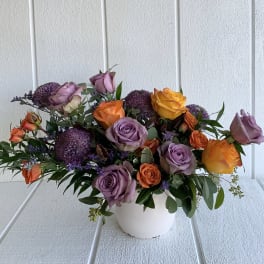 Mixed rose arrangement in a white vase with purple accents