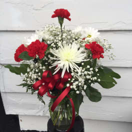 Bouquet of red carnations and white daisies in a glass vase with a red ribbon