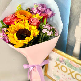 Bouquet of sunflowers, roses, and purple flowers wrapped in pink paper