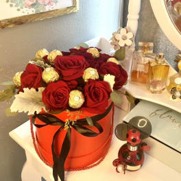Red roses and gold-wrapped chocolates arranged in a round orange box