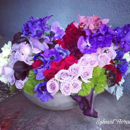 Colorful floral arrangement in a low bowl with roses and purple blooms