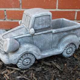 Gray pickup truck-shaped planter on mulch in front of a brick wall