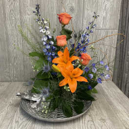 Orange lilies and roses arranged in a silver tray with a small alligator figurine.