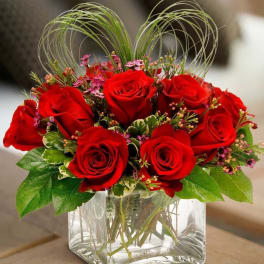 Red roses arranged in a clear square glass vase with decorative loops
