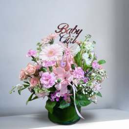 Pink floral arrangement in a green vase with a "Baby Girl" topper