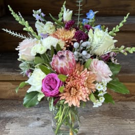 Mixed bouquet of pink, peach, white, and blue flowers in a glass vase