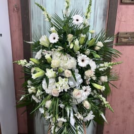 Large white funeral spray with lilies, roses, and daisies on an easel