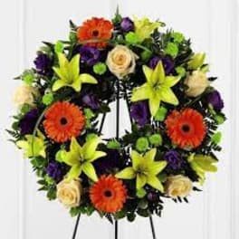 Circular floral wreath with orange gerberas, yellow lilies, cream roses, and purple blooms