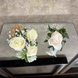 Two white rose boutonnieres with baby's breath and greenery