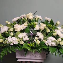 White floral arrangement in a decorative rectangular planter with a clear cross centerpiece