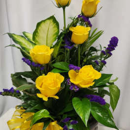 Yellow roses and purple filler flowers arranged in a decorative vase