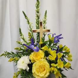 Yellow roses and purple flowers arranged around a gold cross