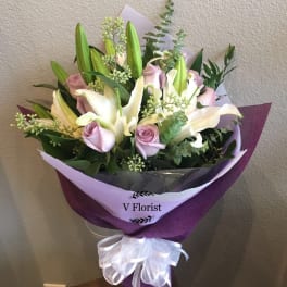 Bouquet of white lilies and pale pink roses wrapped in purple paper