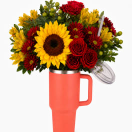 Bouquet of red and yellow flowers in a coral tumbler vase with lid and straw