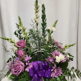 Purple and white floral arrangement in a clear cross vase with a purple ribbon