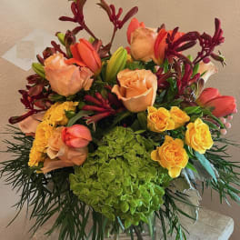 Mixed bouquet of peach roses, yellow roses, and red tulips in a glass vase