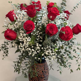 Red roses arranged in a decorative vase with baby's breath and eucalyptus