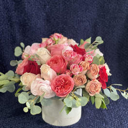 Pink and red roses arranged in a white round box with eucalyptus