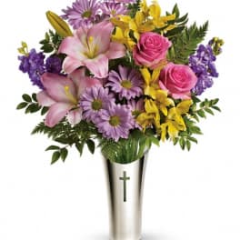 Bouquet of pink lilies, roses, and purple daisies in a silver vase with a cross