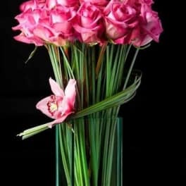 Pink roses arranged in a tall glass vase with one orchid bloom