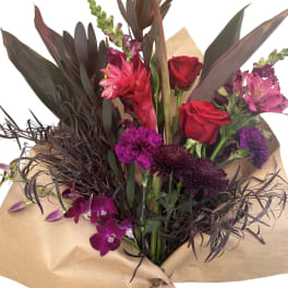 Bouquet of red roses, purple orchids, and dark foliage wrapped in kraft paper