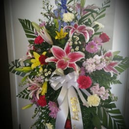 Tall mixed flower standing spray with lilies, roses, and a white ribbon