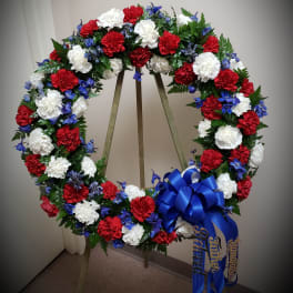Red, white, and blue floral wreath on a stand with a ribbon bow