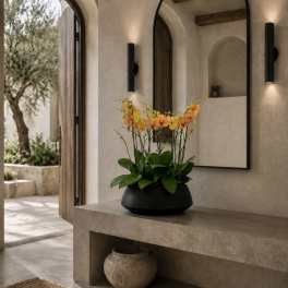 Orange and yellow orchids in a black bowl on a stone console