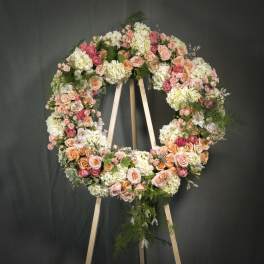 Large standing wreath of peach and pink roses with white hydrangeas on a wooden easel