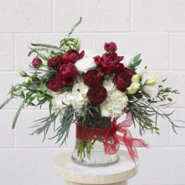 Red and white floral arrangement in a glass vase with a red ribbon