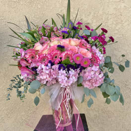 Large pink and purple floral arrangement in a glass vase with ribbon