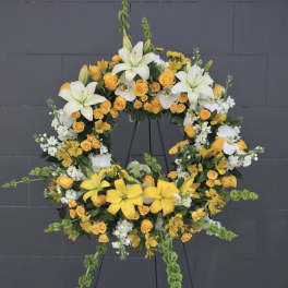Circular floral wreath with white lilies, yellow roses, and white filler flowers