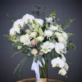 White orchids and roses in a tall glass vase with a ribbon